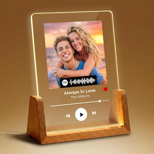 May include: A clear acrylic plaque with a wooden base featuring a printed photograph of a couple, a Spotify-style music player interface, a sound wave graphic, the text Always in Love and The Wilsons, a red heart icon, and playback controls.