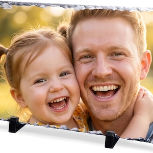 May include: A rectangular photo slate plaque featuring a color photograph of a smiling adult and a young child with their heads pressed together. The plaque has a natural, rough, chipped stone edge and is supported by two black plastic stands.