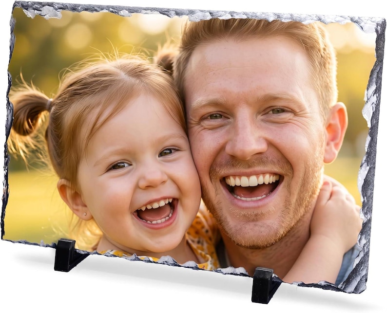 May include: A rectangular photo slate plaque featuring a color photograph of a smiling adult and a young child with their heads pressed together. The plaque has a natural, rough, chipped stone edge and is supported by two black plastic stands.