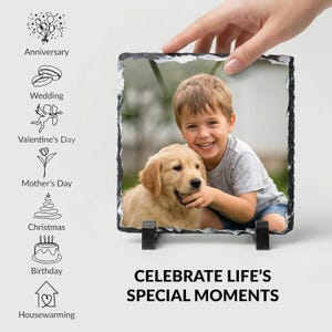 May include: A square slate photo plaque with rough, chiseled edges featuring a color photograph of a young child and a golden retriever puppy. The plaque is displayed on two black plastic stands and includes text reading CELEBRATE LIFE'S SPECIAL MOMENTS.
