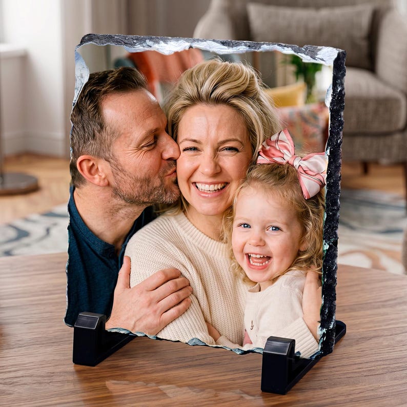 May include: A rectangular photo slate plaque featuring a printed image of a family of three. The plaque has rough, jagged, dark gray stone edges and is supported by two black plastic stands. The image shows a man, a woman, and a young child.