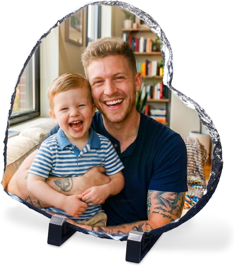 May include: A heart-shaped slate photo plaque featuring a printed image of a smiling adult and a young child. The plaque has a rough, natural stone edge and is supported by two black plastic stands positioned at the base of the heart shape.