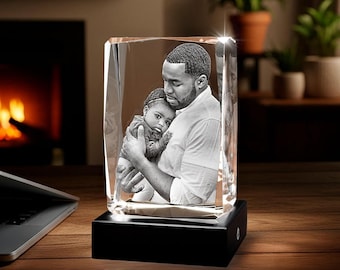 May include: A rectangular crystal block featuring a laser-etched black and white photograph of an adult holding a small child. The clear glass block sits on a solid black rectangular base, creating a reflective and transparent display piece.