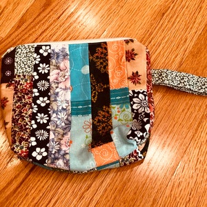 May include: A small patchwork fabric pouch with a zipper closure and a fabric handle. The pouch is made of various colorful fabrics with floral patterns.