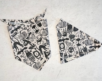 May include: Two black and white patterned dog bandanas with a Halloween theme. The bandanas feature various spooky characters like bats, cats, pumpkins, and spiders. The larger bandana has the text "The Woof Dog Co."