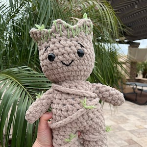 May include: A crocheted plush toy of Groot from Guardians of the Galaxy. The toy is brown with green accents and has a friendly expression.