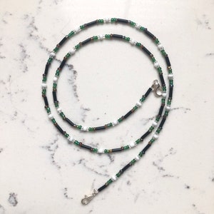 May include: A black, white, and green beaded chain with silver clasps. The chain is made of small round beads and larger rectangular beads.