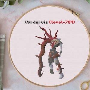 May include: Cross-stitch embroidery of a pixelated character, Vardorvis, with the text "Vardorvis (level-784)". The character is in a wooden embroidery hoop. The design features shades of red, brown, gray, and white.