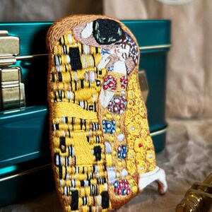 May include: A hand-stitched embroidered patch depicting Gustav Klimt's "The Kiss" painting. The patch features a yellow, gold, and black color scheme with intricate details.