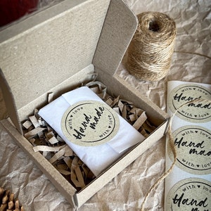 May include: A small cardboard box with a white tissue paper inside. The box is filled with brown crinkled paper. The box has a sticker on it that says "Hand made with love".