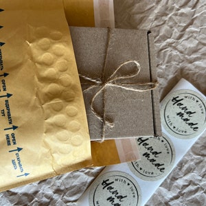 May include: Three round, brown paper stickers with the text "Hand made with love" in black script. The stickers are on a white background.