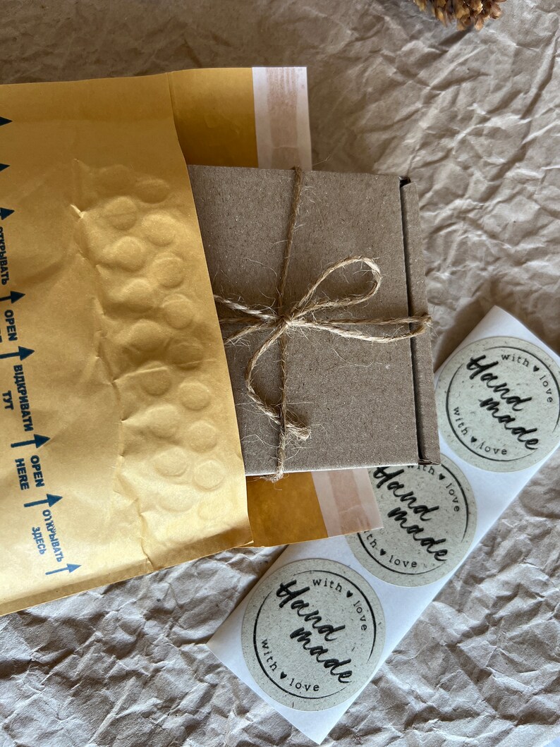 May include: Three round, brown paper stickers with the text "Hand made with love" in black script. The stickers are on a white background.