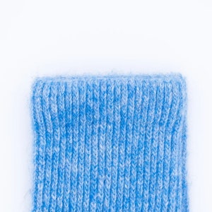 Puede incluir: Primer plano del pu&ntilde;o de un calcet&iacute;n de punto azul claro. El pu&ntilde;o es acanalado y tiene un aspecto suave y texturizado. El calcet&iacute;n est&aacute; hecho de un hilo azul claro con motas blancas, creando un efecto jaspeado. El fondo es blanco liso.