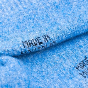 Puede incluir: Primer plano de calcetines azul claro con el texto "MADE IN USA" impreso en negro en el pu&ntilde;o. Los calcetines tienen un aspecto texturizado y una costura visible.