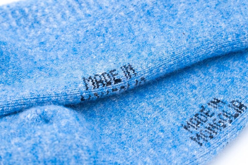 Puede incluir: Primer plano de calcetines azul claro con el texto "MADE IN USA" impreso en negro en el pu&ntilde;o. Los calcetines tienen un aspecto texturizado y una costura visible.