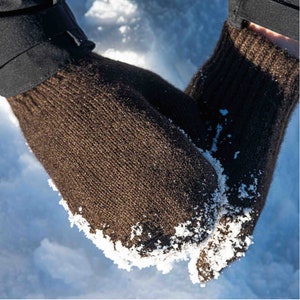 May include: A pair of brown knitted gloves with a textured surface. The gloves are covered in small white snow flakes.