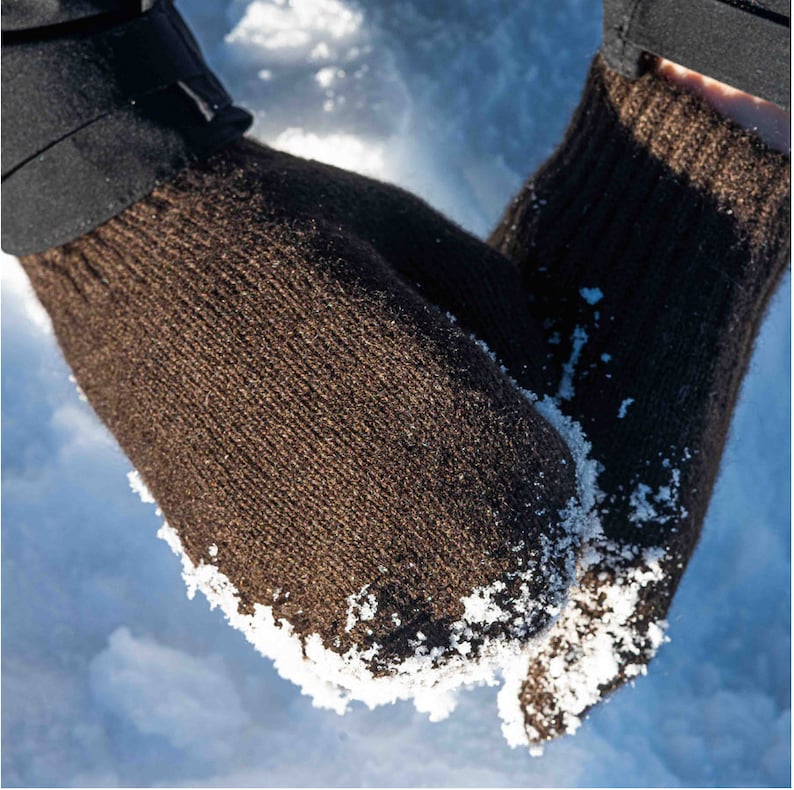 May include: A pair of brown knitted gloves with a textured surface. The gloves are covered in small white snow flakes.