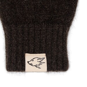 May include: A pair of brown knitted gloves with a small, cream-colored label featuring a black and white illustration of a fox's head.