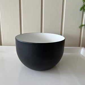 Puede incluir: Un tazón negro con interior blanco. El tazón es redondo y tiene una superficie lisa.