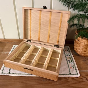 May include: A wooden box with a hinged lid and a compartment for storing small items. The box is made of light wood and has a natural finish. The lid is open and the compartment is visible. The compartment is divided into several sections.