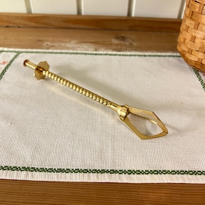 May include: A gold-coloured metal sugar tong with a textured handle and a diamond-shaped opening at the end.