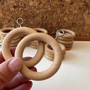 K&ouml;nnte beinhalten: Nahaufnahme von Holz-Vorhangringen mit einem Metallhaken. Die Ringe sind gestapelt und hellbraun.