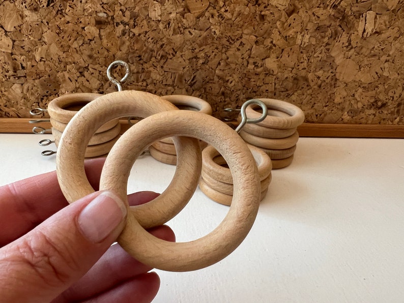 K&ouml;nnte beinhalten: Nahaufnahme von Holz-Vorhangringen mit einem Metallhaken. Die Ringe sind gestapelt und hellbraun.