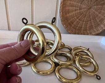 May include: A set of 10 gold metal curtain rings with a small loop on each ring. The rings are arranged in a pile on a white surface.