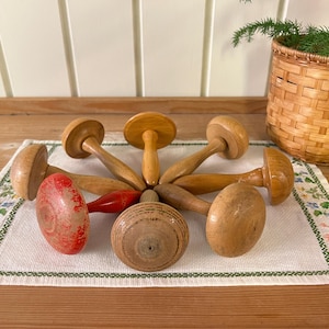 May include: Seven wooden thimbles with red and natural wood finishes. The thimbles are arranged in a circle on a white fabric with a floral pattern.