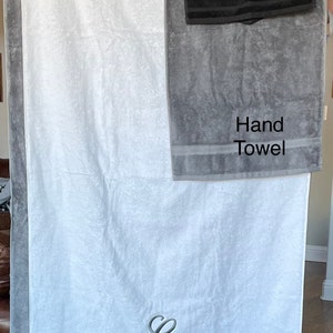 May include: A set of four towels in various sizes, including a washcloth, hand towel, bath towel, and bath sheet. The towels are gray and white with a gray border and the word "Wash Cloth", "Hand Towel", "Bath Towel", and "Bath Sheet" printed on each towel. The towels are hanging on a clothesline.