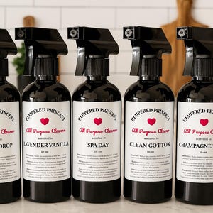May include: Five black spray bottles of "Pampered Princess All Purpose Cleaner" with white labels and black text. Scents include Lemon Drop, Lavender Vanilla, Spa Day, Clean Cotton, and Champagne Toast. Each bottle is 296 ml.