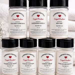 May include: A collection of eight carpet freshener bottles with black lids. Each bottle is labeled "Pampered Princess" and features a heart logo. The scents include Volcano Capri Blue, Lavender Vanilla, Spa Day, Champagne Toast, Clean Cotton, Lemon Drop, and Pink Sugar Crystal.