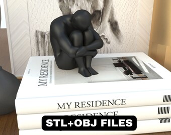 Pode incluir: Uma escultura preta de uma pessoa sentada com os joelhos puxados para o peito. A escultura está sentada em cima de uma pilha de três livros. O livro superior tem o título "MY RESIDENCE" impresso na capa. O livro inferior tem o texto "STL+OBJ FILES" impresso na capa.