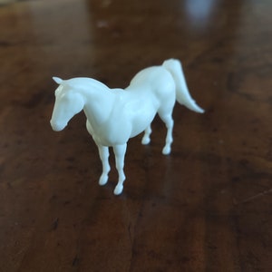 May include: A white plastic horse figurine. The horse is standing on all four legs with its head lowered.