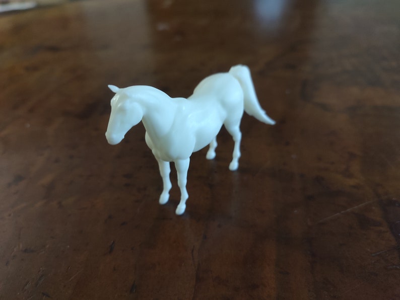 May include: A white plastic horse figurine. The horse is standing on all four legs with its head lowered.