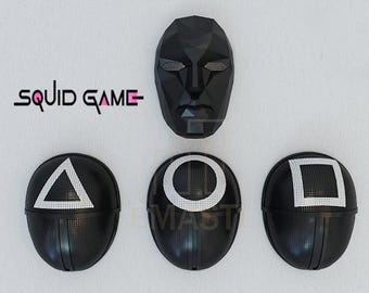 Pode incluir: Três máscaras pretas com diferentes formas geométricas: um triângulo, um círculo e um quadrado. Cada forma é contornada em branco. As máscaras são da popular série da Netflix "Squid Game".