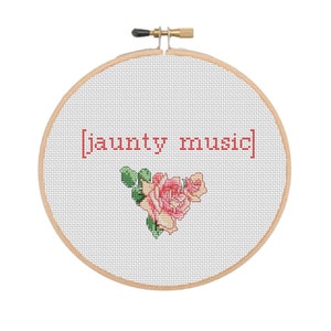 Könnte beinhalten: Ein weißer Stickrahmen mit einem roten Kreuzstich-Design, auf dem "[jaunty music]" steht, und einem rosafarbenen und grünen Blumendesign.
