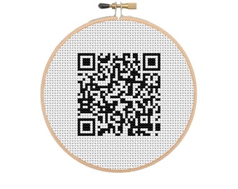 May include: A cross-stitch hoop featuring a black and white QR code design. The QR code is centered on a white fabric background, framed by a natural wood hoop. The design is a modern take on traditional needlework.
