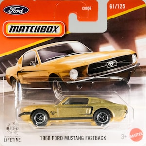 May include: A gold 1968 Ford Mustang Fastback die-cast toy car in its original blister pack packaging. The card features a graphic of the car, the Matchbox logo, the Ford logo, and the text 61/125, C0859, and Designed for a Lifetime.