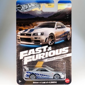Puede incluir: Un coche de juguete Hot Wheels de metal plateado, modelo Nissan Skyline GT-R (BNR34) de la franquicia Fast & Furious. El coche tiene rayas de carreras azules y blancas y las palabras "Fast & Furious" y "Brian O'Conner" están impresas en el embalaje.