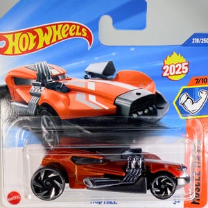 May include: Orange and black Hot Wheels toy car with silver accents. The car has large wheels and a unique design, with the text "Hot Wheels" visible at the top. The packaging includes the number "2025" and the text "Muscle Mania".