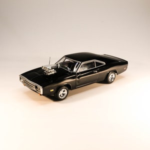 Op de afbeelding: Een zwart model van een klassieke muscle car. De auto heeft een verchroomd motoronderdeel, chromen wielen en een glanzende afwerking. Het model is een gedetailleerde replica van een vintage voertuig, dat het iconische ontwerp laat zien.