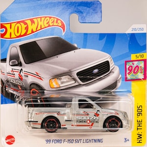 Può includere: Un'auto giocattolo Hot Wheels argentata di una '99 Ford F-150 SVT Lightning. Il camion ha ruote nere e rosse e il testo "SOUZA PLUMBING HEATING" sul lato. La confezione include il testo "HW: THE '90S" e "210/250".