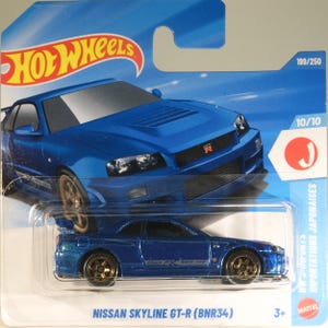 Op de afbeelding: Een blauwe Hot Wheels Nissan Skyline GT-R (BNR34) gegoten speelgoedauto in de originele blauw-witte blisterverpakking. De verpakking bevat het Hot Wheels-logo, de tekst 199/250, 10/10 en de modelnaam van de auto onderaan gedrukt.