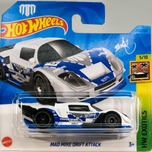 May include: A Hot Wheels die-cast car, the "Mad Mike Drift Attack" model, is displayed in its original packaging. The car features a white and blue design with sponsor logos. The packaging is blue and green, with the Hot Wheels logo and "HW Exotics" branding.