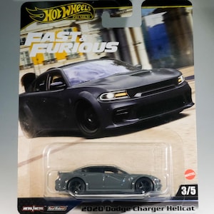 Op de afbeelding: Een Hot Wheels modelauto van een 2020 Dodge Charger Hellcat, uit de Fast & Furious serie. De auto is donkergrijs met zwarte wielen en zit in een doorzichtige plastic verpakking. De verpakking toont het Hot Wheels logo en de tekst "Fast & Furious".