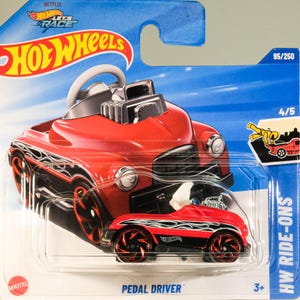 May include: A red Hot Wheels Pedal Driver toy car with black and silver accents. The car is packaged in a blue and white card with the Hot Wheels logo and Netflix branding. The car is 4/5 in the series.