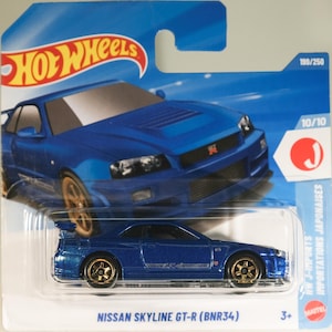 Puede incluir: Un coche de juguete Hot Wheels Nissan Skyline GT-R (BNR34) azul en su embalaje original de blíster azul y blanco. El embalaje presenta un gráfico del coche, el logotipo de Hot Wheels y el texto 199/250, 10/10 y HW J-IMPORTS.