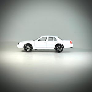 May include: A white toy sedan with black wheels and tires. The car has a four-door design with a red taillight. The vehicle is a miniature replica of a full-size car.