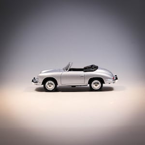 May include: A silver convertible toy car with a black hood. The miniature vehicle has a classic design, featuring round headlights and wheels. The car is a die-cast model, likely made of metal, and is displayed on a neutral background.